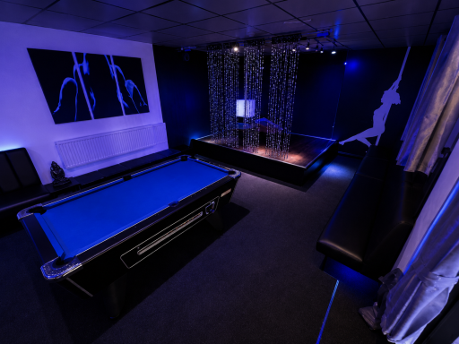 A dimly lit room featuring a blue pool table and a stage with curtains.