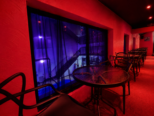 Interior of a dimly lit venue with red walls, tables, and purple-lit curtains.