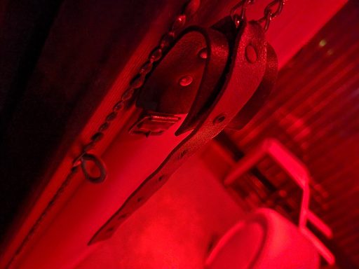 Metal locks hang from chains in a dimly lit, red-toned environment.