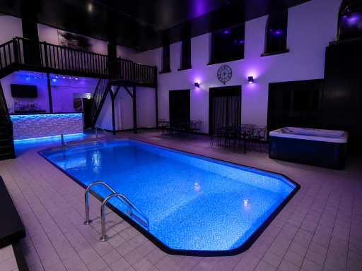 Indoor swimming pool with blue lighting and a hot tub.